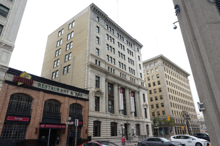 The Great West Life building surrounded by other buildings. Parked vehicles are in front.