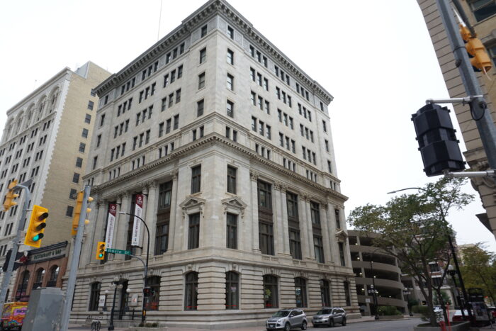 The Great West Life building with vehicles parked alongside it. Stoplights with a sign reading “Rorie St” are in front.