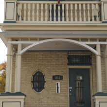 Image 2: The front yellow-brick facade and entrance with an overhanging balcony.