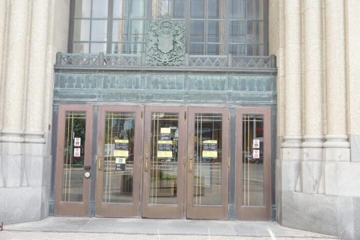 Entrée principale du bâtiment fédéral avec trois portes. Les armoiries du Canada sont au-dessus de la porte du milieu.  