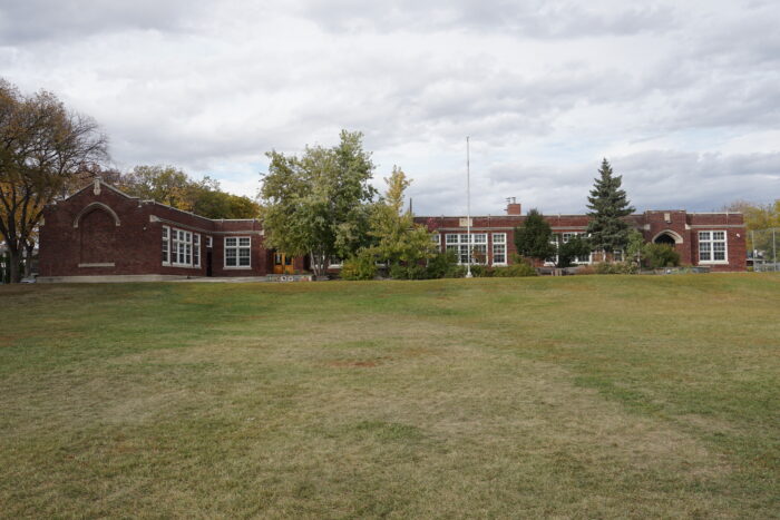 Wolseley School with much of the facade obscured by a flagpole and large trees growing in front.