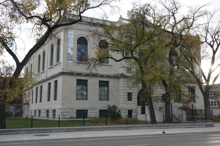 Winnipeg’s Carnegie Library with trees growing in the yard obscuring the facades.