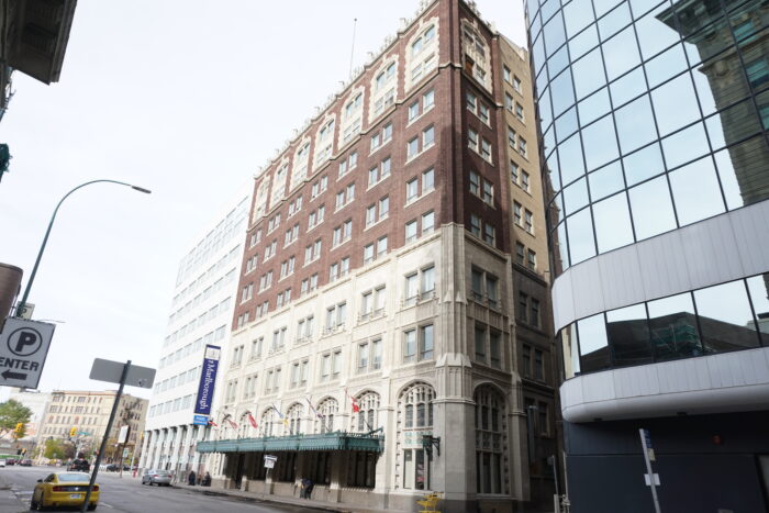 The Marlborough Hotel with a sign reading “The Marlborough” on the facade. People are on the sidewalk in front.