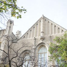 Image 8: Looking up the Knox Church facade from a distance featuring the pointed top with decorative elements on the exterior walls and trees in view