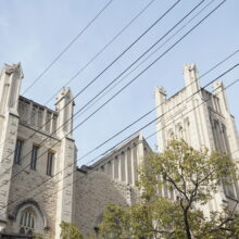 Image 9: Looking up the Knox Church facade from a distance featuring the pointed top with decorative elements on the exterior walls, the two towers that flank the main structure and trees in view