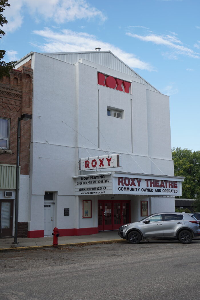 Roxy Theatre with an SUV parked in front. Marquee reads “Roxy Theatre: Community Owned and Operated.”