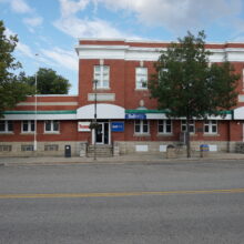 Imag_1 The Neepawa Post Office with “Neepawa Building” displayed on the front facade. A tree grows in front of it.