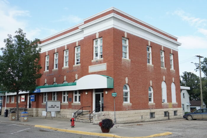 The Neepawa Post Office with “Neepawa Building” displayed on the front facade. A tree grows in front of it.