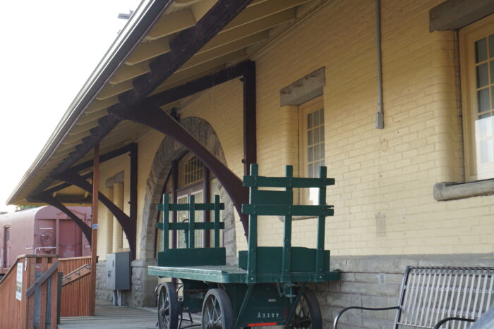 Portage La Prairie’s Canadian Pacific Railway Station. A bench and antique luggage cart sit on the verandah in front.