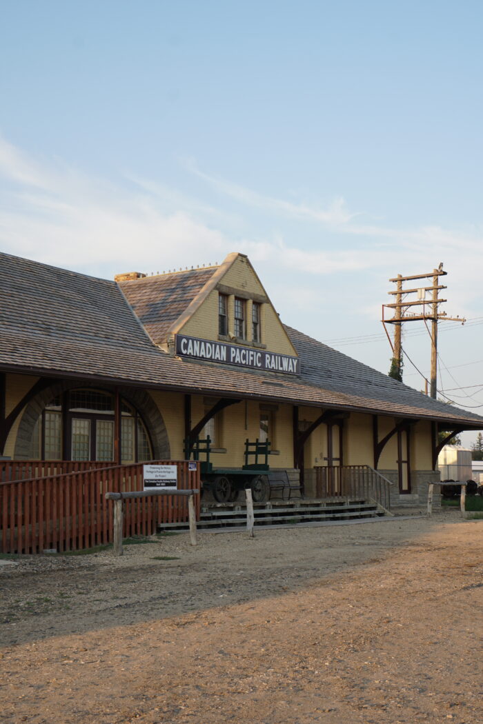 Portage La Prairie’s Canadian Pacific Railway Station. A bench and antique luggage cart sit on the verandah in front.