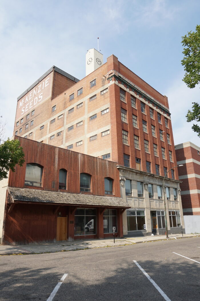 The McKenzie Building with a clock tower above. Advertising on the side of the building reads “McKENZIE SEEDS.”