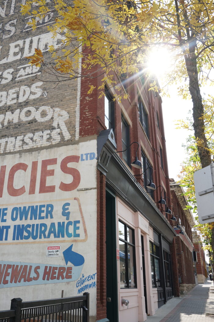 The Campbell & Campbell Building with advertising painted on the side. The sun shines through a tree in front.