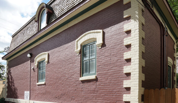 A red brick exterior wall with two stone arched windows and decorative Quoin on right corner