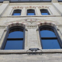 Image 1: Looking up the facade of the Macdonald Block building featuring arched windows and decorative architectural details on the exterior walls