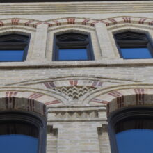 Image 2: Looking up the facade of the Macdonald Block building featuring arched windows and decorative architectural details on the exterior walls