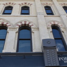 Image 3: Looking up the facade of the Macdonald Block building featuring arched windows and decorative architectural details on the exterior walls