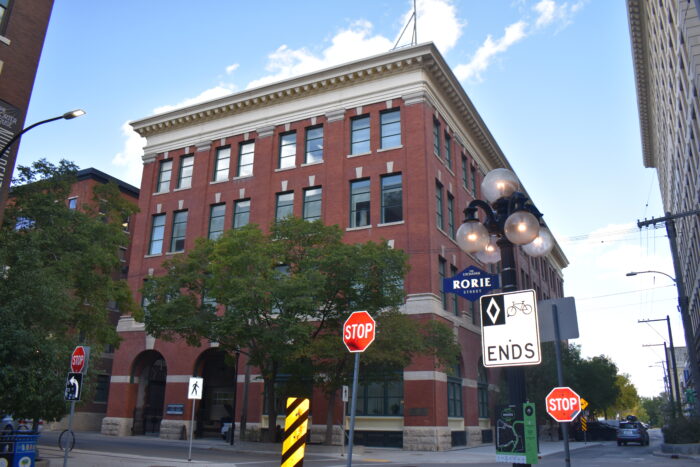 Winnipeg’s Customs Examining Warehouse behind a tree. Various street signs are visible across the foreground.