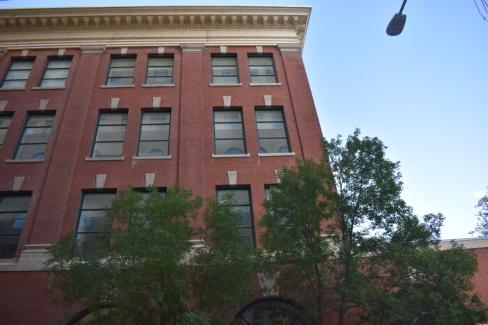 Looking up at the top three storeys of Winnipeg’s Customs Examining Warehouse while trees grow up from below.