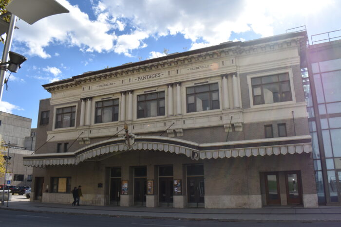 Winnipeg’s Pantages Theatre with the text “UNEQUALLED PANTAGES VAUDEVILLE” on the front facade. Two people walk by.