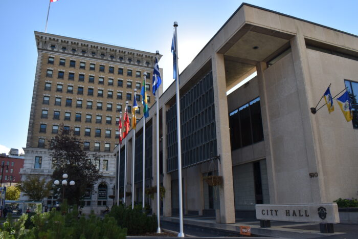 Winnipeg’s City Hall Council Building with a row of flags in front. A sign next to it reads “CITY HALL.”