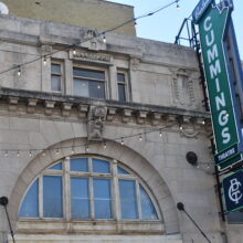 Image 3: Details on the upper facade of the Walker Theatre building with a sign hanging towards the right side that reads "Burton Cummings Theatre"