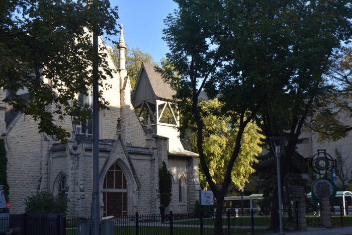 Holy Trinity Church behind a wrought iron fence, partly obscured by trees.