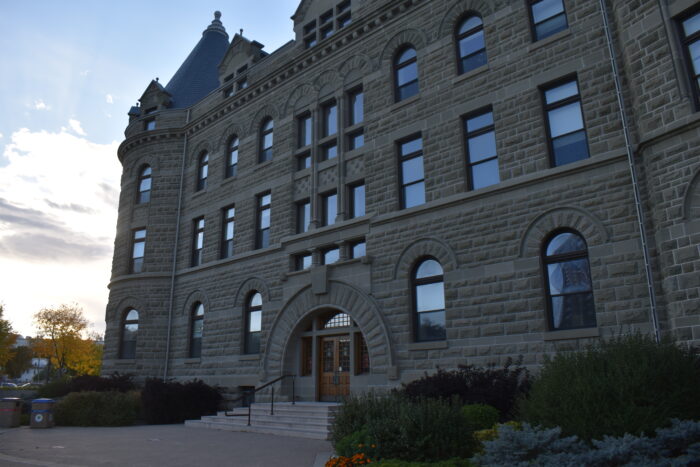 The front facade of Wesley Hall at the University of Winnipeg with landscaping and garbage cans in front.