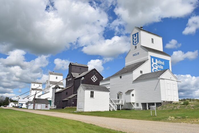 Four grain elevators along a road in Inglis. The elevator in the foreground reads “UUG” and “INGLIS.”