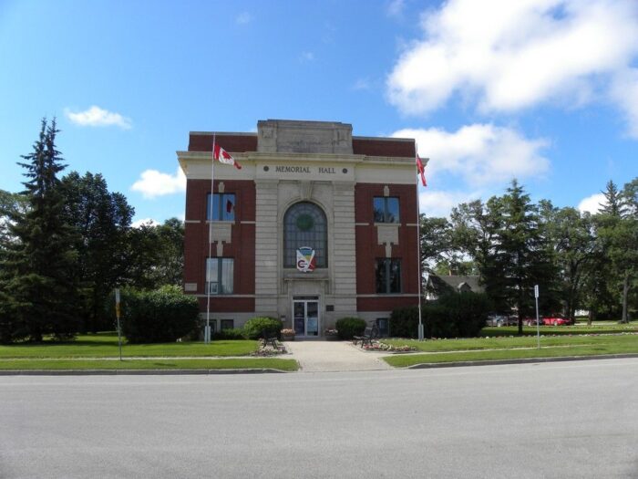 A Canadian flag flies on a flagpole in front of the Carman Memorial Hall.