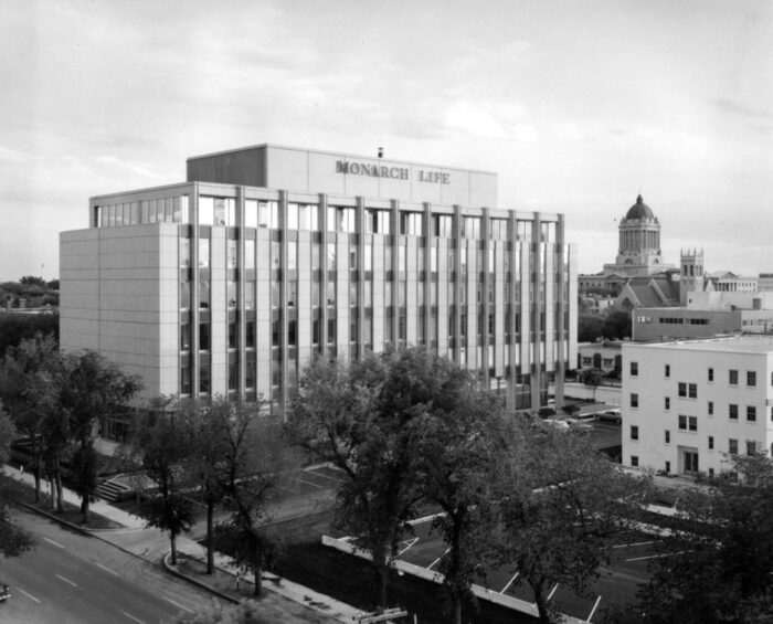 The Monarch Life Building with the Manitoba Legislative Building in the background. Trees obscure part of the facade.