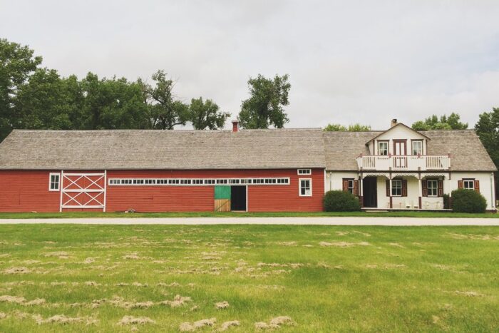 The Friesen Housebarn with two shrubs growing in front of the house. A mowed lawn is in the foreground.