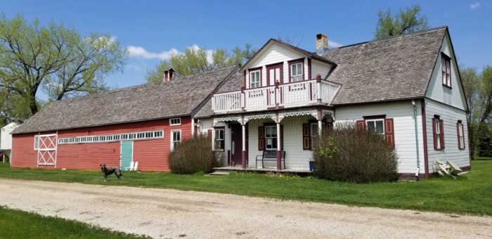 The Friesen Housebarn with various lawn furniture along the building. A dog stands in front of the barn.