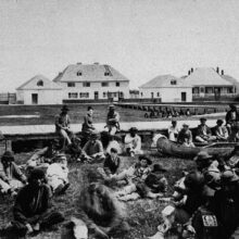 Image 2: A crowd of indigenous people gathered on lawn across from Norway House buildings.