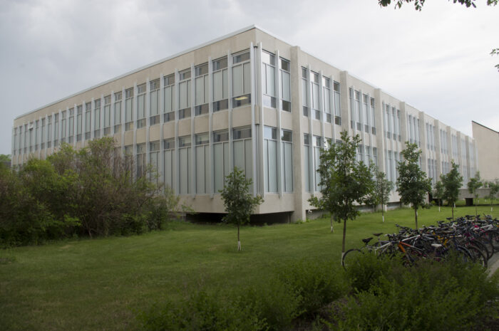 The John A. Russell Building with trees and a bike rack full of bikes in front.