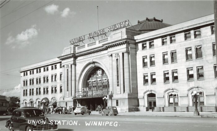 Winnipeg’s Union Station with a sign reading “CANADIAN NATIONAL RAILWAYS” along the roofline. Vehicles and people are in front.