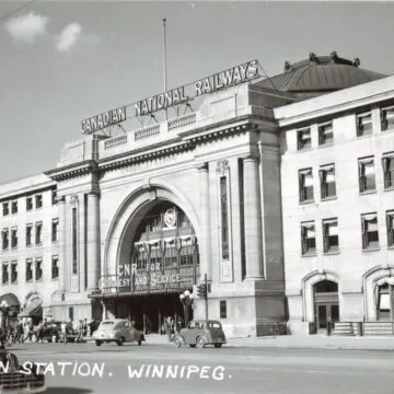 Winnipeg’s Union Station with a sign reading “CANADIAN NATIONAL RAILWAYS” along the roofline. Vehicles and people are in front.