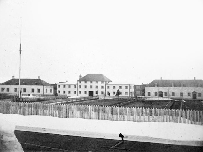 Three York Factory buildings behind a wooden fence. An anchor lies in front of the fence.